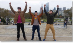 three guys standing with hands up in front of a city landscape